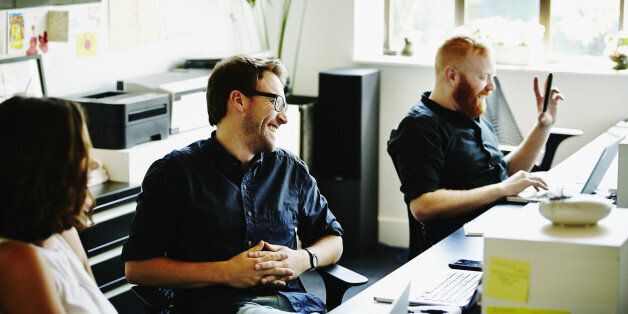 Laughing coworkers sitting at workstations in startup office discussing project