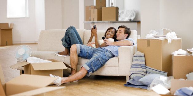 A young couple relaxing on a sofa and texting after moving into a house.