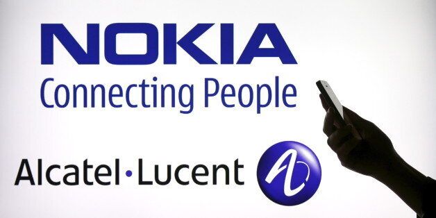 A woman holds a smartphone in front of a screen displaying both Nokia and Alcatel Lucent logos in this photo illustration in Paris, April 14, 2015. Nokia Oyj is in talks to buy Alcatel-Lucent, a deal that could create a European telecoms equipment group worth over 40 billion euros ($42 billion), and cut costs at two of the industry's weaker players. REUTERS/Benoit Tessier