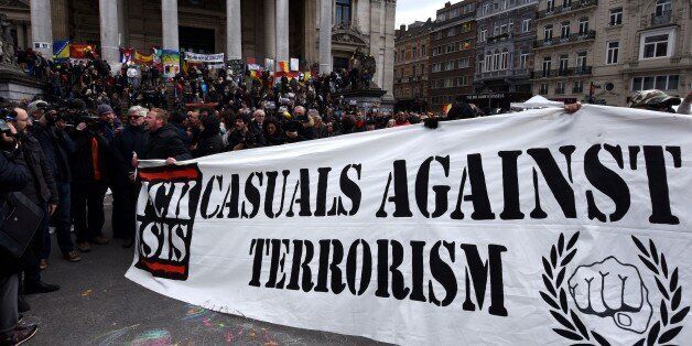 A group of people march behind a banner of the 'FCK-Casuals' hooligan movement, as they arrive in the square outside the stock exchange in Brussels on March 27, 2016 as tensions mounted after the square was invaded by some 200 far-right football hooligans. Police fired water a cannon at far-right football hooligans who invaded a square in the Belgian capital that has become a memorial to the victims of the Brussels attacks, an AFP journalist said. Police took action after about 200 black-clad hooligans shouting nationalist and anti-immigrant slogans moved in on the Place de la Bourse where people were gathering in a show of solidarity with the victims. / AFP / PATRIK STOLLARZ (Photo credit should read PATRIK STOLLARZ/AFP/Getty Images)