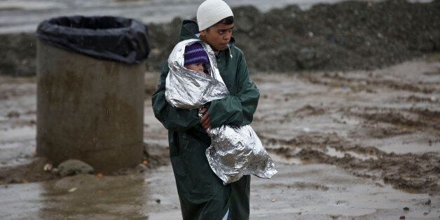 A migrant holds a baby covered in a thermal blanket at a makeshift camp at the northern Greek border station of Idomeni, Sunday March 13, 2016. Bad weather returned after a brief pause and conditions in the refugee camp on the Greek-Macedonian where about 14,000 people are stranded have further deteriorated, many of its residents struggling to cope with the many challenges posed by the heavy rain. (AP Photo/Visar Kryeziu)