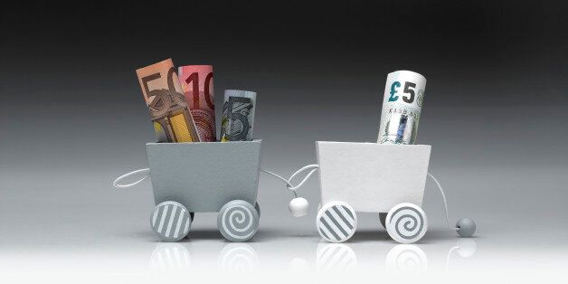 Detail of a toy train, consisting of two wooden wagons. The wagons are connected between them and they are shot on a gradient background. One wagon is pulling the other. The wagons are carrying euros and pounds in banknotes. The photograph was shot in a studio and its frame is horizontal.