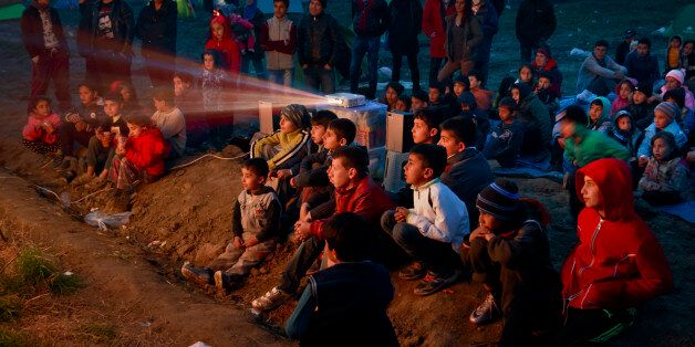 Children watch a cartoon movie in a field at the northern Greek border station of Idomeni, Saturday, March 5, 2016. The regional governor of the Greek region of Central Macedonia called on the Greek government Saturday to declare a state of emergency for the area surrounding the Idomeni border crossing saying that up to 14,000 people are trapped in Idomeni, while another 6,000-7,000 are being housed in refugee camps around the region, meaning the area was handling about 60 percent of the total number in the country. (AP Photo/Vadim Ghirda)