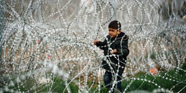 TOPSHOT - A child stands among a razor-topped fence close to the gate at the Greek-Macedonian border near the Greek village of Idomeni, on March 7, 2016, where thousands of migrants and refugees wait to cross the border into Macedonia.EU leaders held a summit with Turkey's prime minister on March 7 in order to back closing the Balkans migrant route and urge Ankara to accept deportations of large numbers of economic migrants from overstretched Greece. / AFP / DIMITAR DILKOFF (Photo credit should read DIMITAR DILKOFF/AFP/Getty Images)