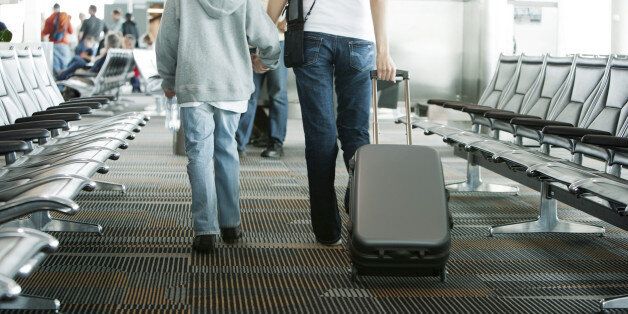 Mother and son walking in airport, mother pulling suitcase, rear view