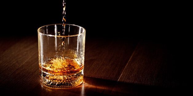 Scotch or bourbon whiskey (or whisky) being poured into a glass with dramatic studio lighting and a black background.