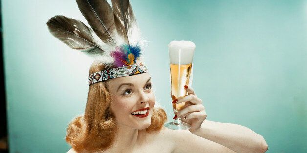 Young woman wearing feather headdress, holding beer glass