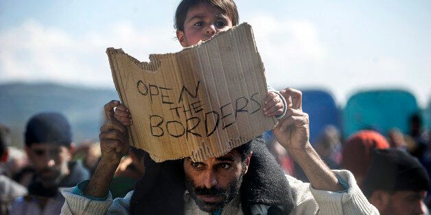 A man carries on his shoulders a child holding a banner reading 'Open the borders' during a demostration of migrants and refugees protesting behind a fence and barbed wire at the Greek-Macedonian border, near Gevgelija, on February 27, 2016.Macedonia denied all passage to Afghans and ramped up document controls for Syrians and Iraqis. On February 26, there were some 4,000 people waiting to cross at the border post of Idomeni, local police said. Greek authorities have been regulating the flow of refugees but hundreds have set out on foot for the border, determined to continue their journey despite being told they will be turned back. / AFP / Robert ATANASOVSKI (Photo credit should read ROBERT ATANASOVSKI/AFP/Getty Images)