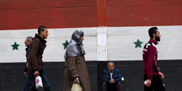 Syrians walk past a shop with a painting of the national flag in Damascus, Syria, Tuesday, Feb. 23, 2016. The Syrian government and the main umbrella for Syrian opposition and rebel groups announced on Tuesday they both conditionally accept a proposed U.S.-Russian cease fire that the international community hopes will bring them back to the negotiating table in Geneva for talks to end the war.(AP Photo/Hassan Ammar)