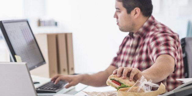 Mixed race businessman eating and working at desk