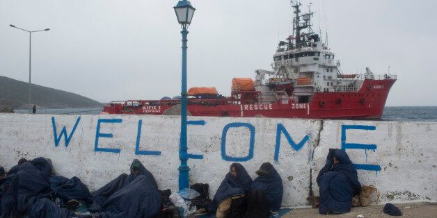 In this photo taken on Wednesday, Jan. 20, 2016, refugees and migrants are covered with sleeping bags during a rainfall at the Greek island of Oinousses, as at the background is docked a large privately-owned tug converted into a rescue boat to transport them to Chios island. Hour after hour, by night and by day, Greek coast guard patrol and lifeboats, reinforced by vessels from the European Unionâs border agency Frontex, ply the waters of the eastern Aegean Sea along the frontier with Turkey, on the lookout for people being smuggled onto the shores of Greek islands - the frontline of Europeâs massive refugee crisis. (AP Photo/Petros Giannakouris)