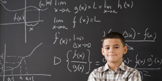 Hispanic boy smiling in front of math formula on blackboard