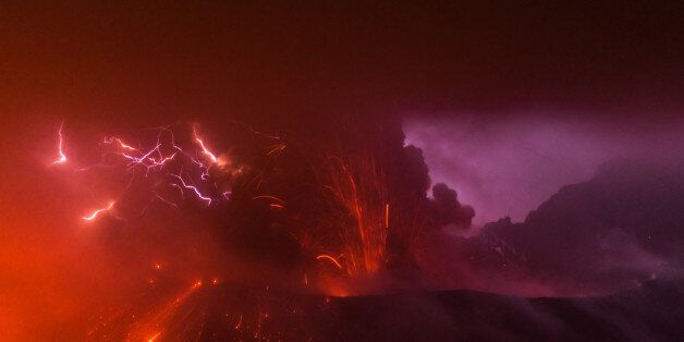 Sakurajima volcano erupts at night, producing dense ash, volcanic lightning and ejecting red hot glowing bombs from the Showa crater.