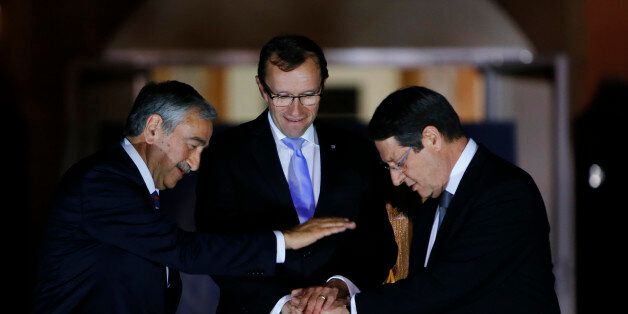 FILE - In this Monday, May 11, 2015 file photo, Cyprus' President Nicos Anastasiades, right, Turkish Cypriot leader Mustafa Akinci, left, and United Nations envoy Espen Barth Eide shake hands after a dinner at the Ledra Palace Hotel inside the UN controlled buffer zone that divides the Cypriot capital Nicosia. A peace accord cobbling Cyprus back together again after more than four decades of ethnic division will bring opportunity and economic growth, officials say _ and it could also carry a heavy financial burden. The challenges of melding the separate economies of an internationally recognized Greek Cypriot south that enjoys full European Union membership benefits and a breakaway Turkish Cypriot north that relies heavily Turkeyâs financial support are coming into sharp relief as the tiny island nationâs rival leaders carry on with tough negotiations into the new year. Cyprus was split in 1974 when Turkey invaded after a coup by supporters of union with Greece. (AP Photo/Petros Karadjias, File)