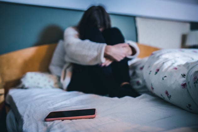 Stock image of distressed young woman sitting on a bed with phone in the foreground. 