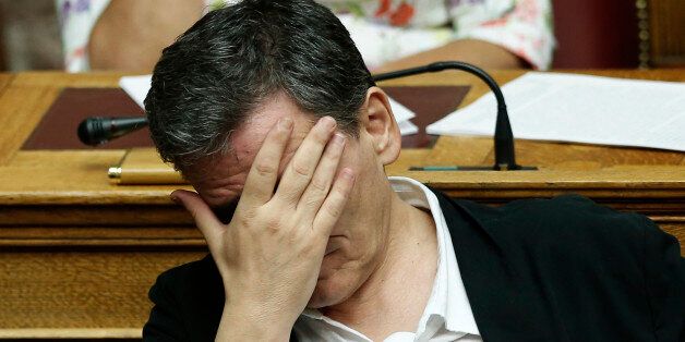 Greek Finance Minister Euclid Tsakalotos covers his face during a parliamentary session in Athens, early Friday, Aug. 14, 2015. The Greek government defended its new bailout program in tumultuous parliamentary sessions as it faced a rebellion in the governing Syriza party ahead of a vote on the deal. (AP Photo/Yannis Liakos)