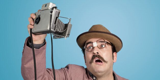 Portrait of nerd photographer taking a selfie with an old fashioned camera over blue background.