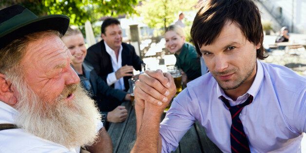 Germany, Bavaria, Upper Bavaria, Two men arm wrestling in beer garden, friends in background
