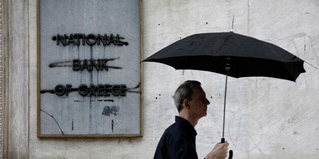A pedestrian passes a graffiti damaged sign at the entrance to a main branch of the National Bank of Greece SA in Thessaloniki, Greece, on Wednesday, July 1, 2015. Even those payments risked putting more pressure on banks than they could bear, underscoring the desperate choices facing the six-month-old left-wing government and voters in the referendum. Photographer: Konstantinos Tsakalidis/Bloomberg via Getty Images