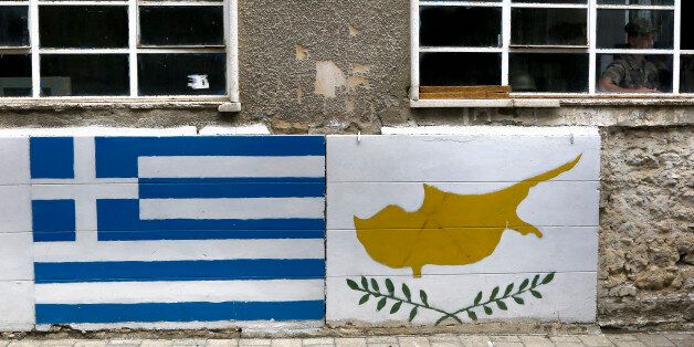 A representation of the Greek, left, and Cyprus flags are painted on a wall as a Greek Cypriot soldier is seen inside a guard post by the U.N controlled buffer zone as they cuts across the Cypriot divided capital Nicosia on Thursday, May 14 2015. Cyprus President Nicos Anastasiades and Turkish Cypriot leader Mustafa Akinci, stalled talks aimed at reunifying ethnically divided Cyprus will resume Friday, May 15. Cyprus was split in 1974 when Turkey invaded after a coup by supporters of union with Greece. (AP Photo/Petros Karadjias)
