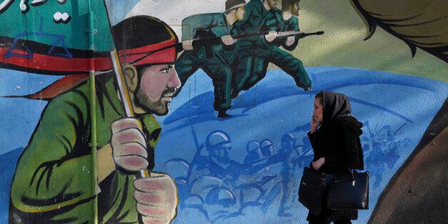 An Iranian woman walks past a mural depicting Iranian armed forces in the battlefield, at Palestine Sq. in Tehran, Iran, Saturday, Jan. 16, 2016. The end of Western sanctions against Iran loomed Saturday as Iran's foreign minister suggested the U.N. atomic agency is close to certifying that his country has met all commitments under its landmark nuclear deal with six world powers. (AP Photo/Vahid Salemi)