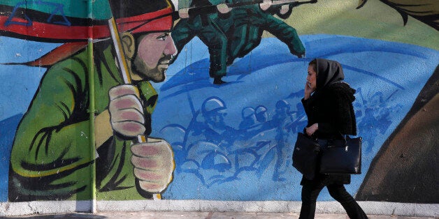 An Iranian woman walks past a mural depicting Iranian armed forces in the battlefield, at Palestine Sq. in Tehran, Iran, Saturday, Jan. 16, 2016. The end of Western sanctions against Iran loomed Saturday as Iran's foreign minister suggested the U.N. atomic agency is close to certifying that his country has met all commitments under its landmark nuclear deal with six world powers. (AP Photo/Vahid Salemi)