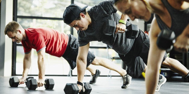 Group of friends doing pushups with dumbbells in crossfit gym