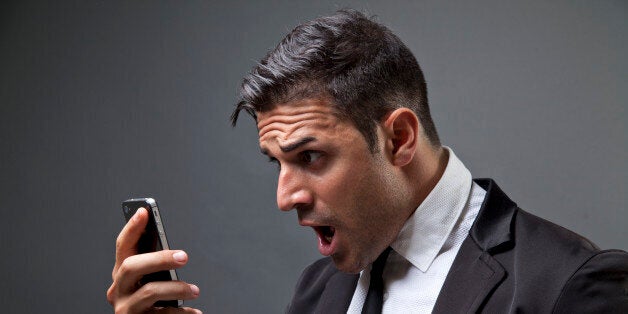 Hombre vestido de traje y corbata, mirando un mensaje en el mÃ³vil con cara de asombro y gritando.