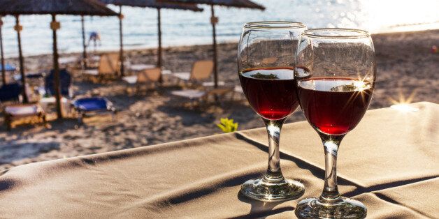 Two glasses with red wine with sun reflection, sea, sunset on beach at the background. Summertime vacation concept
