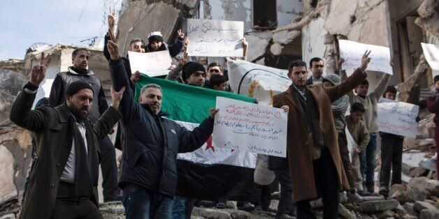 Syrians hold banners amid rubble during a demonstration on January 10, 2016 in the northern city of Aleppo in solidarity with the besieged town of Madaya. Madaya, home to 42,000 people, has become notorious in recent days because of people starving in the town. / AFP / KARAM AL-MASRI (Photo credit should read KARAM AL-MASRI/AFP/Getty Images)