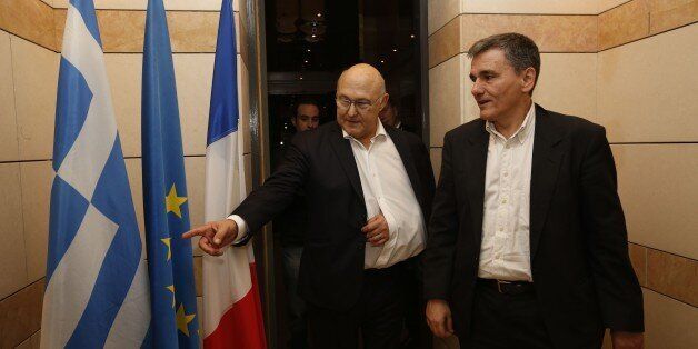 French Finance minister Michel Sapin (C) shows the Greek flag as he welcomes his Greek counterpart Euclide Tsakalotos (R) on January 10, 2016 during a meeting in Paris. / AFP / MATTHIEU ALEXANDRE (Photo credit should read MATTHIEU ALEXANDRE/AFP/Getty Images)