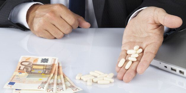 Unrecognisable businessman or office worker on his desk with a bunch of pills and fifty euro banknotes - concept of healthcare and pharmaceutical industry, corruption