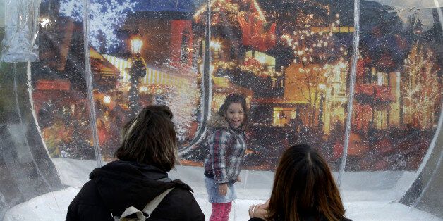 A little girl stands in a plastic globe containing fake snow, as she smiles at two women standing outside, in Athens' festively decorated Klathmonos Square, on Monday, Dec. 23, 2013. Debt-crippled Greece is gearing up for its fourth austerity Christmas, amid hopes that 2014 may see a token return to economic growth after a six-year depression that has seen unemployment exceed 27 percent and left thousands depending on food handouts. (AP Photo/Thanassis Stavrakis)