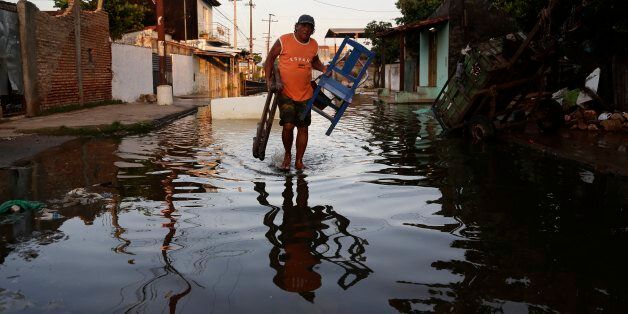 Saturnino Zorrilla carries chairs from his flooded home to a shelter in Asuncion, Paraguay, Wednesday, Dec. 23, 2015. The Paraguay River is at its highest level since 1984 and threatening the poor districts that surround the capital, forcing about 100,000 residents to shelters. (AP Photo/Jorge Saenz)