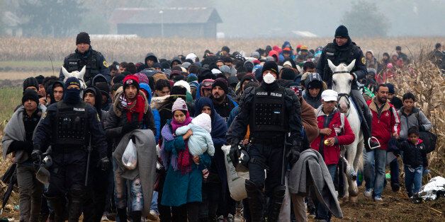 Escorted by police, migrants move through fields after crossing from Croatia, in Rigonce, Slovenia, Tuesday, Oct. 27, 2015. The European Union is lashing member countries for dragging their feet on providing funds and experts to help manage Europe's biggest refugee emergency in decades. (AP Photo/Darko Bandic)