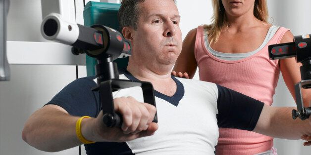 Young female personal trainer by mature man lifting weights