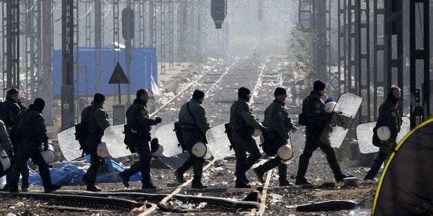 Greek riot police officers walk across railway tracks at Idomeni railway station in northern Greece on the border with Macedonia, photographed from the Macedonian side of the border, near the town of Gevgelija, Wednesday, Dec. 9, 2015. The protest of stranded migrants had severed a key Greek freight train link with northern Europe for three weeks, and also periodically prevented refugees that Macedonia will accept from crossing the border. Some railway services restarted Wednesday after Greek riot police have removed hundreds of protesting migrants from a border crossing to Macedonia. (AP Photo/Boris Grdanoski)