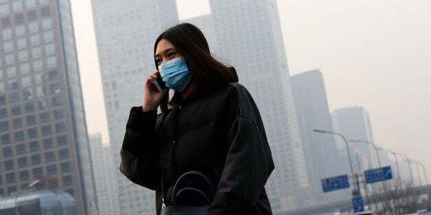 A woman wearing a mask to protect herself from pollutants walks past office buildings shrouded with pollution haze in Beijing, Monday, Dec. 7, 2015. Smog shrouded the capital city Monday after authorities in Beijing issued an orange alert on Saturday. (AP Photo/Andy Wong)