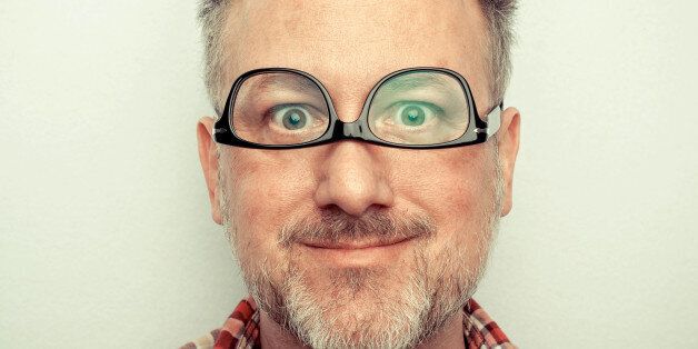 Man wearing glasses upside down, making goofy face. Short hair and grey goatee.