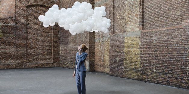 Businesswoman using mobile in empty warehouse with cloud made of balloons above head