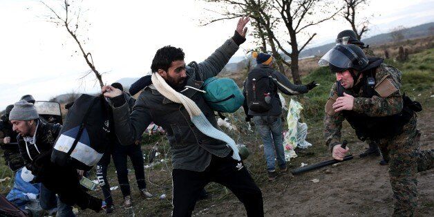 A Macedonian police officer (R) tries to hit a migrant with his baton near Idomeni at the Greek-Macedonian border on November 26, 2015, as migrants and refugees attempted to cross the border. Over 200 migrants on November 26 tried to break through barbed wire fences on Greece's border with Macedonia, throwing stones at riot police. At least three migrants tried to get across in the assault as the crowd shouted 'Open the border' to the Macedonia police ranged across them. AFP PHOTO / ANGELOS TZORTZINIS / AFP / ANGELOS TZORTZINIS (Photo credit should read ANGELOS TZORTZINIS/AFP/Getty Images)