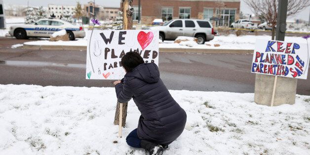 Bethany Winder, a nurse who lives in Colorado Springs, Colo., plants a sign in support of Planned Parenthood just south of its clinic as police investigators gather evidence near the scene of Friday's shooting at the clinic Sunday, Nov. 29, 2015, in northwest Colorado Springs. (AP Photo/David Zalubowski)