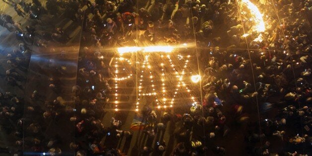 People gather around candles left in the shape of the word 'Peace' reflected through large mirror panels on November 16, 2015 on the old Harbour in Marseille, as thousands of people pay tribute to victims of the November 13 attacks in Paris. Islamic State jihadists claimed a series of coordinated attacks by gunmen and suicide bombers in Paris that killed at least 128 people in scenes of carnage at a concert hall, restaurants and the national stadium. AFP PHOTO / BORIS HORVAT (Photo credit should read BORIS HORVAT/AFP/Getty Images)