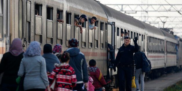 A Croatian police officer helps people board a train at the station in Sid, about 100 km west from Belgrade, Serbia, Tuesday Nov. 3, 2015. Serbia and Croatia have launched a direct train transfer of migrants from one country to another so asylum seekers no longer have to wait long hours outside in the cold. (AP Photo/Darko Vojinovic)