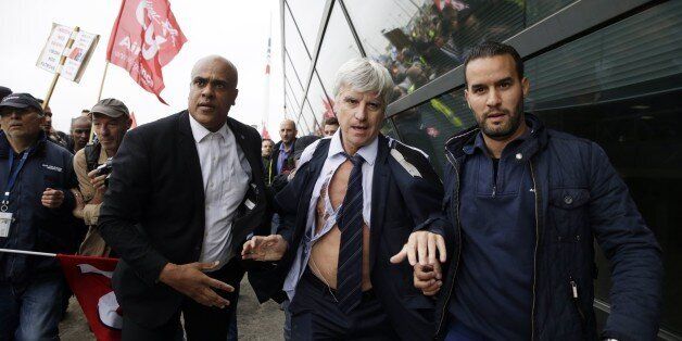 Director in charge of human resources of Air France long-haul flights, Pierre Plissonnier (C), nearly shirtless, runs away from the demonstrators, helped by security officers, after several hundred employees stormed into the offices of Air France, interrupting the meeting of the Central Committee (CCE) in Roissy-en-France, on October 5, 2015. Air France-KLM unveiled a revamped restructuring plan on October 5 that could lead to 2,900 job losses after pilots for the struggling airline refused to accept a proposal to work longer hours. AFP PHOTO / KENZO TRIBOUILLARD (Photo credit should read KENZO TRIBOUILLARD/AFP/Getty Images)