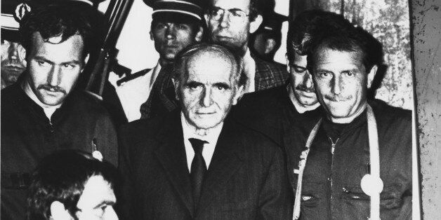 Lyon's, France, Gestapo chief during WW II, Klaus Barbie, is pictured handcuffed as he is led out of the courtroom by heavily armed police officers after he was sentenced to life in prison July 4, 1987 in Lyon, France, for committed crimes against humanity. (AP Photo/Pool)