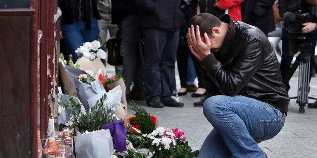 A man holds his head in his hands as he lays flowers in front of the Carillon cafe, in Paris, Saturday, Nov.14, 2015. French President Francois Hollande vowed to attack Islamic State without mercy as the jihadist group admitted responsibility Saturday for orchestrating the deadliest attacks inflicted on France since World War II. (AP Photo/Thibault Camus)