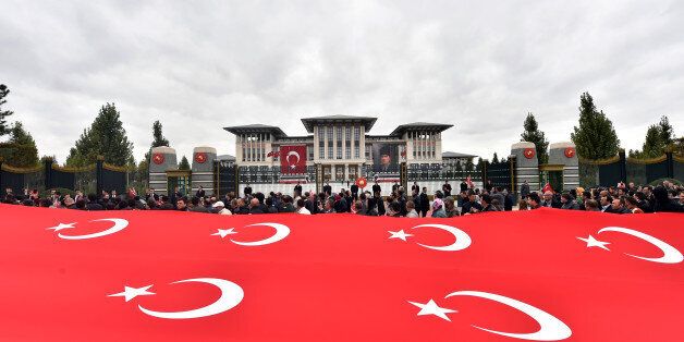 In this Thursday, Oct. 29, 2015 photo made available Friday,Turkish President Recep Tayyip Erdogan, who is barely visible, salutes from a balcony his supporters walking on a main road with national flags outside the gates of his vast presidential palace on Republic Day in Ankara, Turkey. Critics accuse Erdogan of organizing rallies in Turkey and Europe to drum up votes for the ruling Justice and Development Party ahead of Sunday general elections, in breach of laws that require him to be neutral.(AP Photo/Presidential Press Service, Pool )