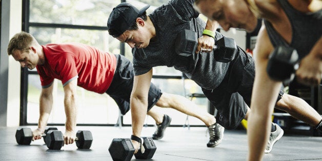 Group of friends doing pushups with dumbbells in crossfit gym