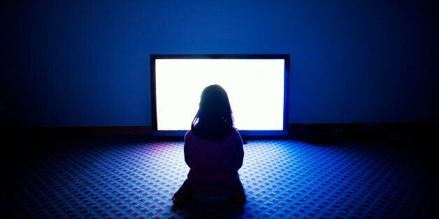 Girl sitting in front of flat screen television in dark room.